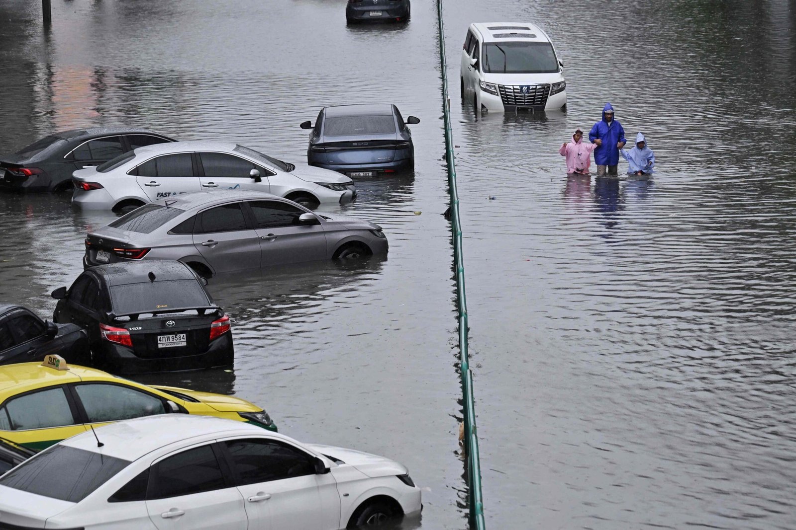 People walk past abandoned vehicles on a flooded Petchaburi road in Bangkok on Saturday. Photo: AFP
